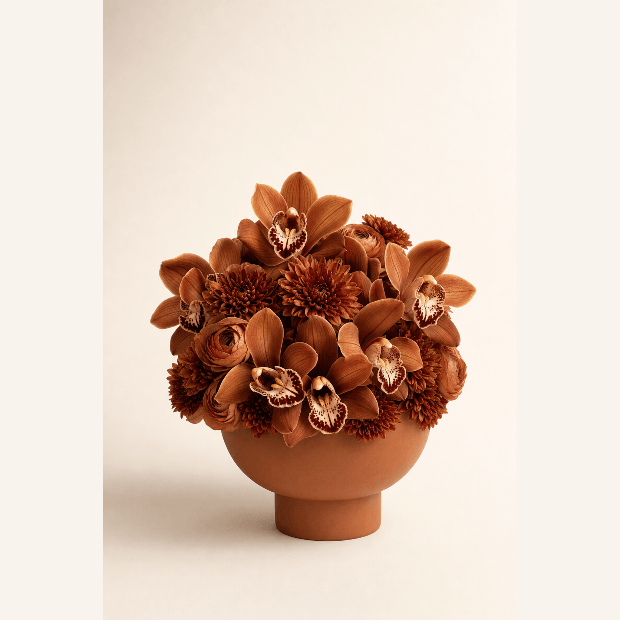 Rust and cream cymbidium orchids, bronze chrysanthemums and terracotta ranunculus in a matte terracotta bowl vase