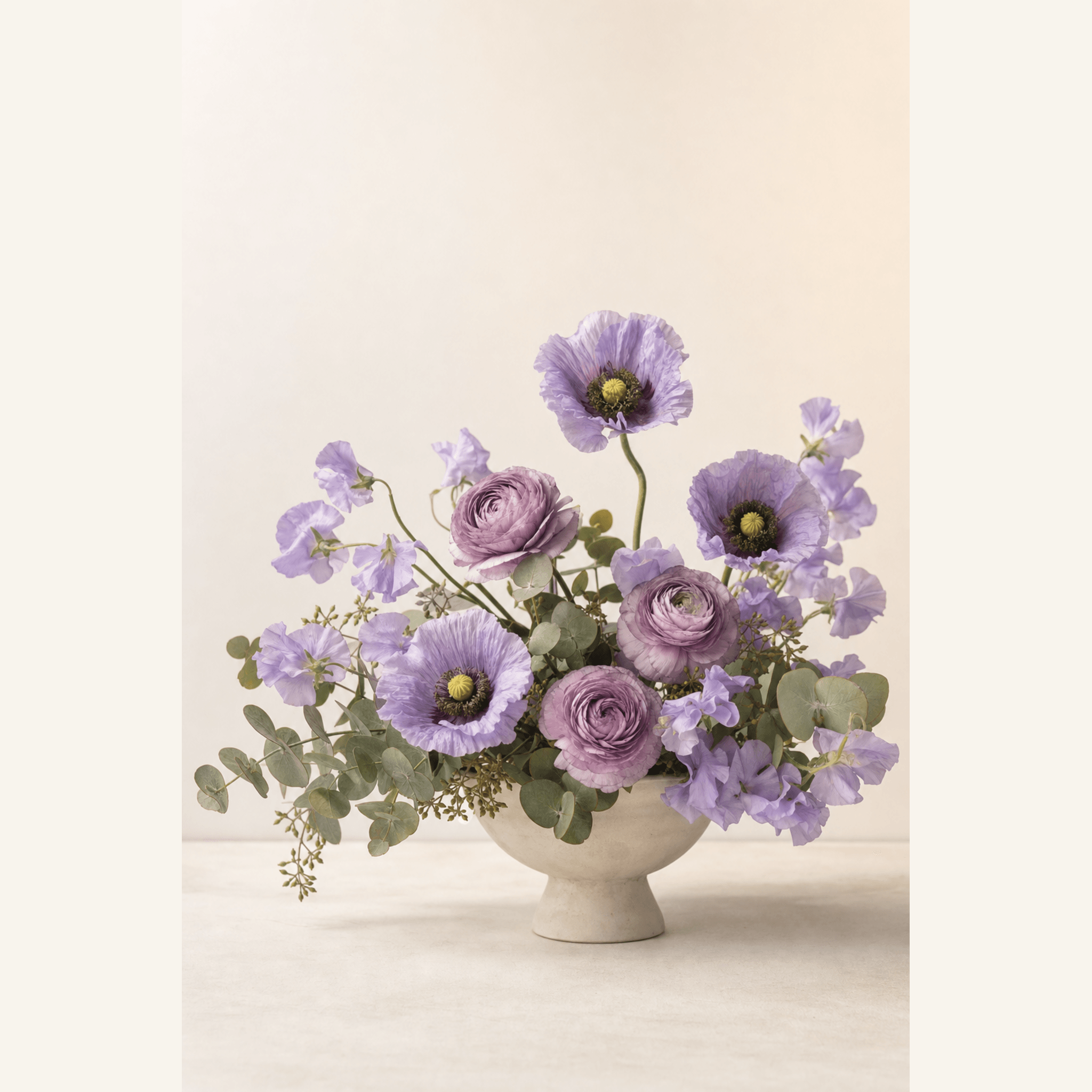 Lavender poppies, mauve ranunculus and sweet peas with eucalyptus in a cream pedestal bowl