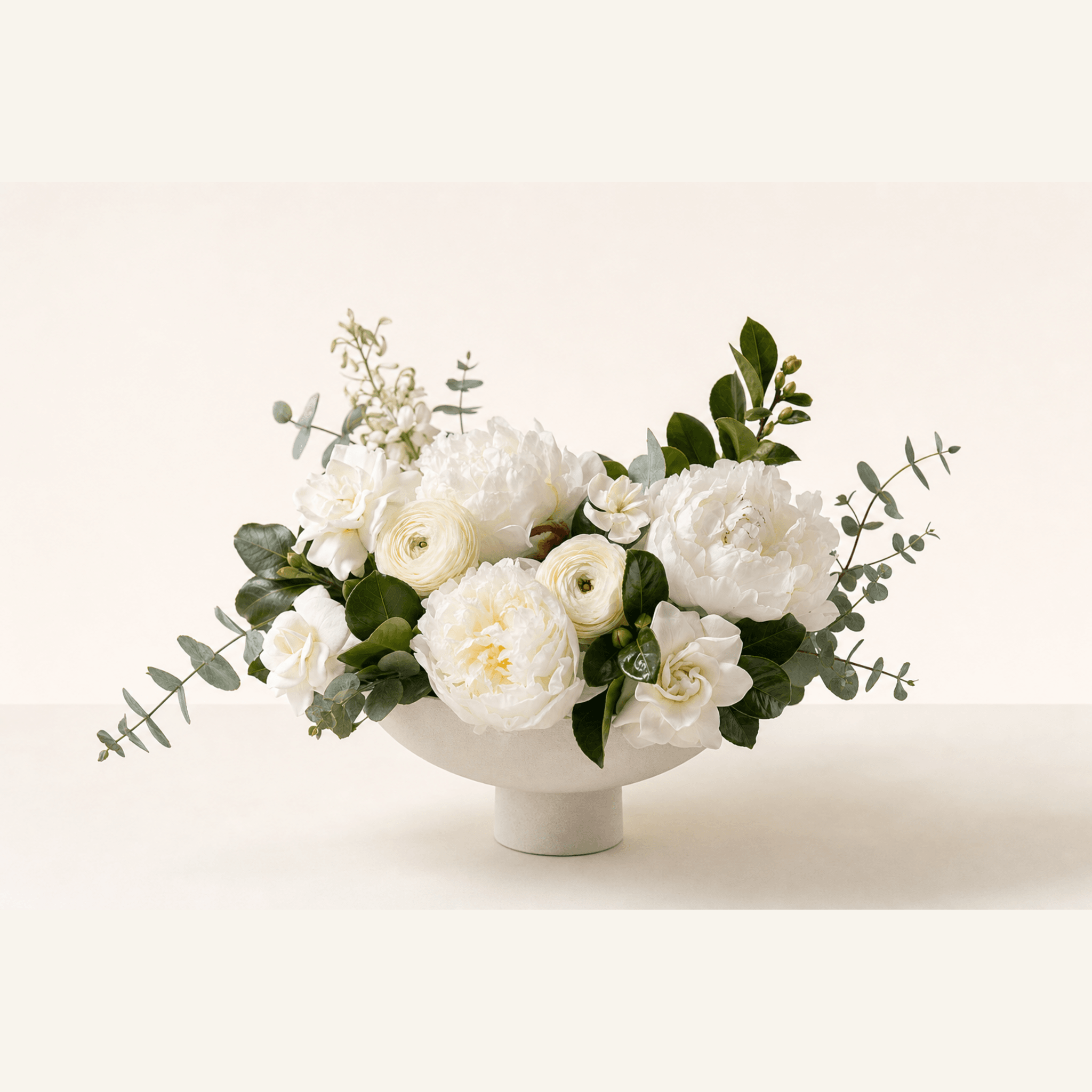 White peonies, garden roses, ranunculus, freesia and eucalyptus in a white pedestal bowl
