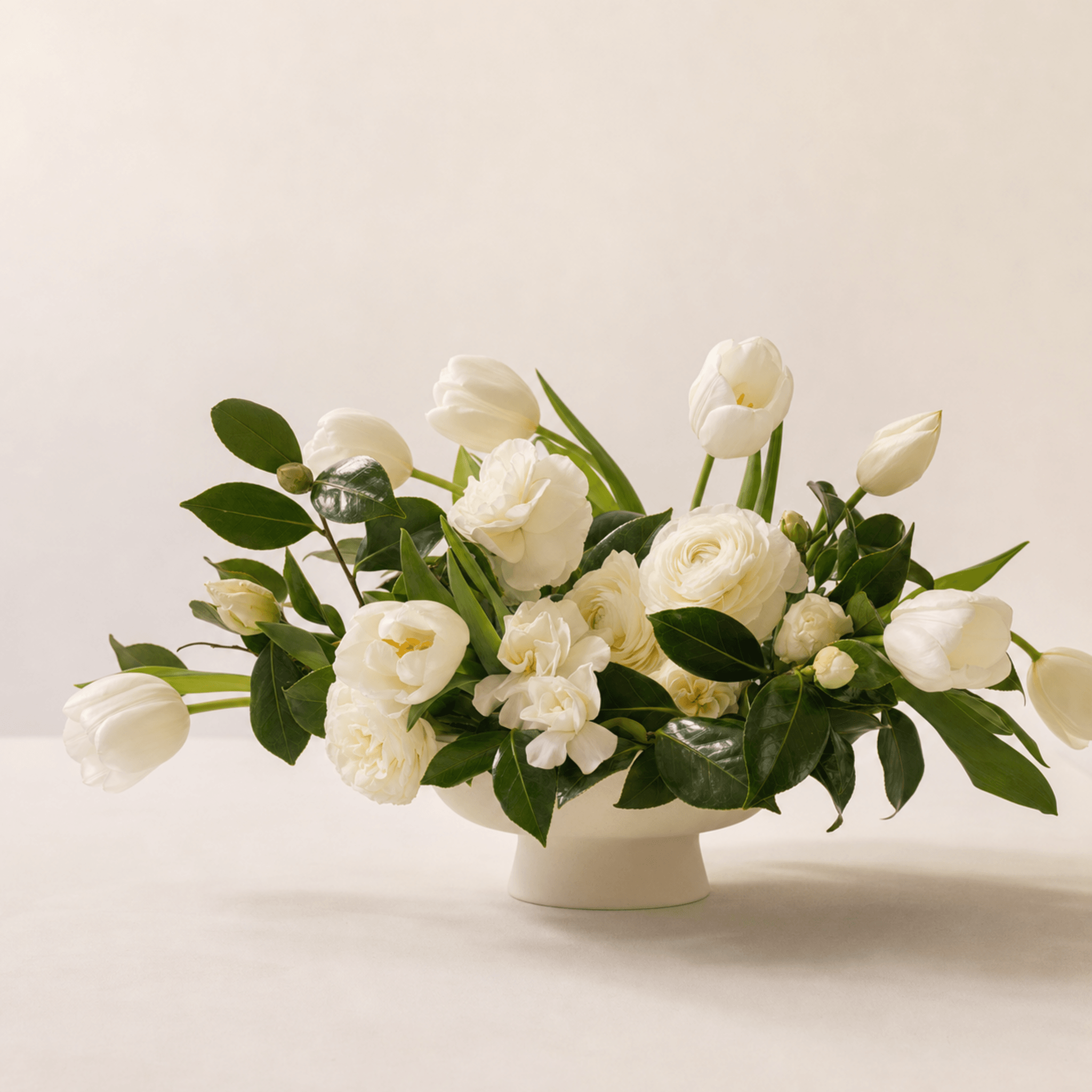 White tulips, ranunculus, garden roses and gardenias arranged in a white ceramic footed bowl